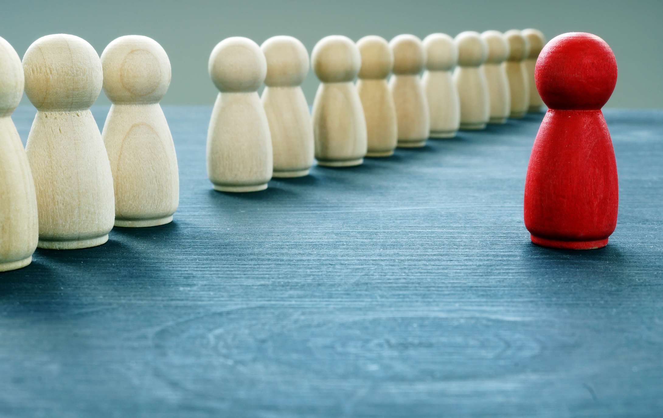 A red, wooden figure stands out from a line of white ones.