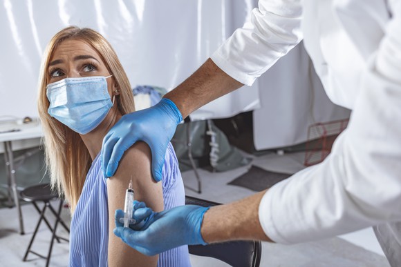 Woman wearing a face mask looking back at a healthcare professional as he gives her a shot in the arm.