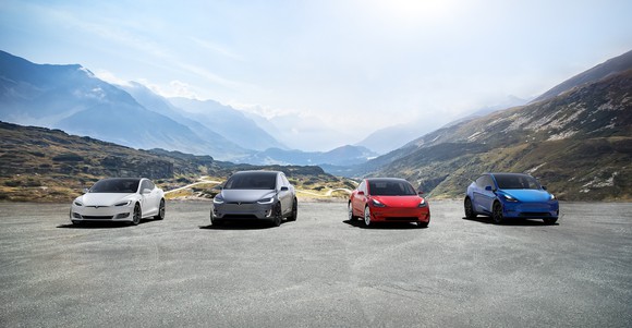 Tesla's Models S, X, 3, and Y lined up on a road with mountains in the background.