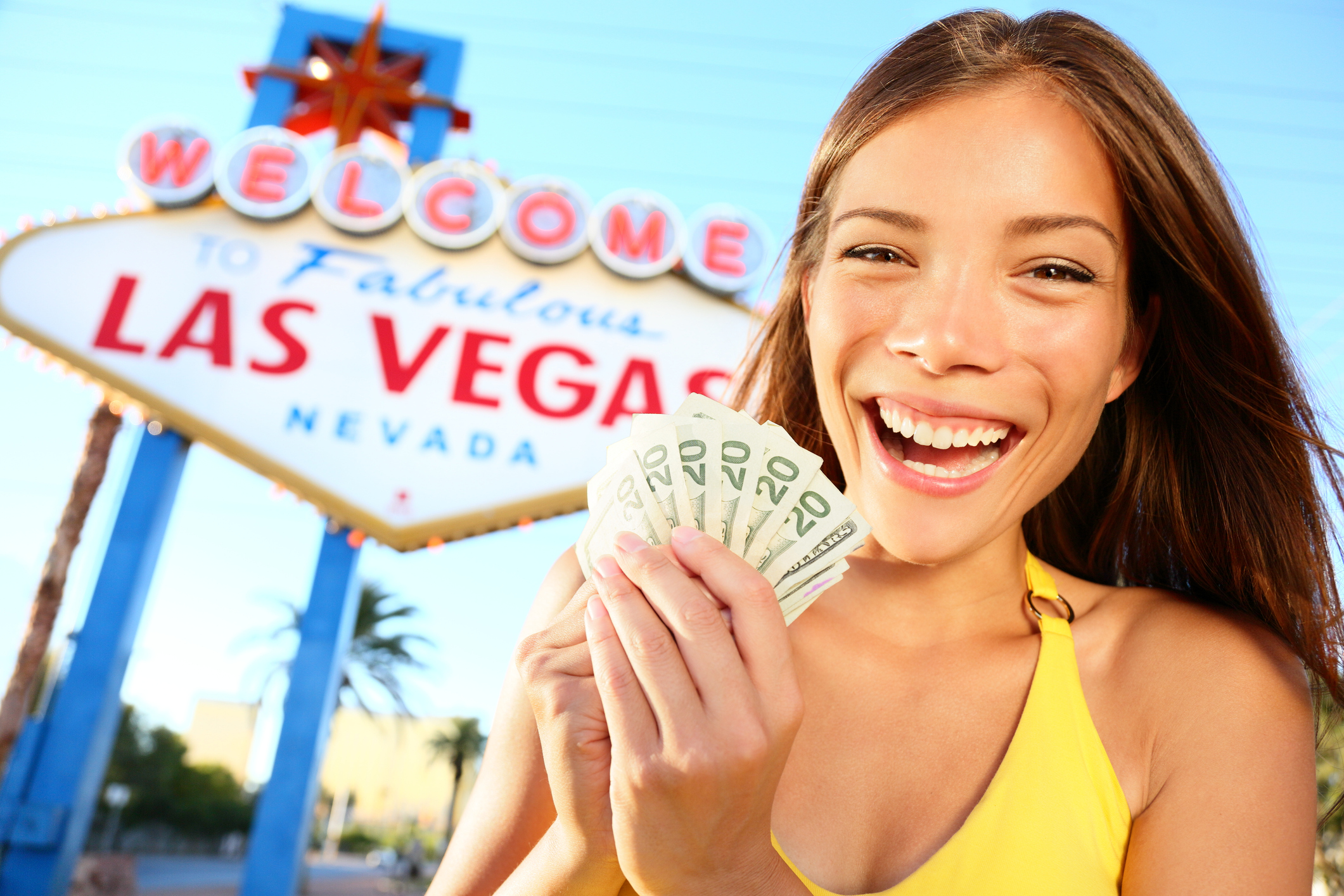 A woman holding a fan of 20-dollar bills in front of a Las Vegas sign.