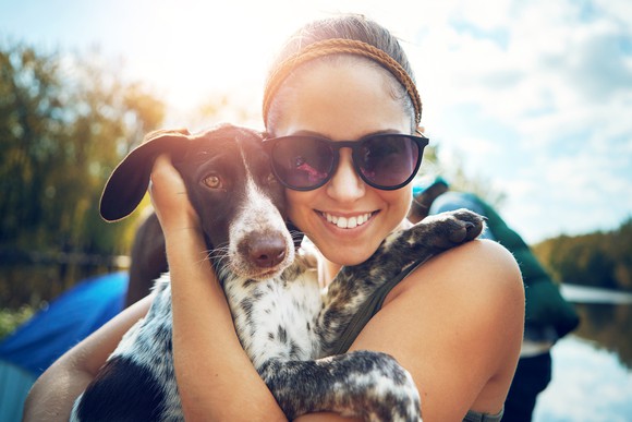 A young woman sitting outside smiles as she cuddles with her dog.