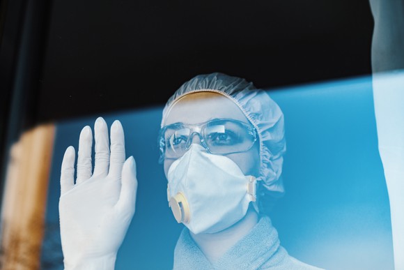 Healthcare worker in personal protective equipment, looking out through a window