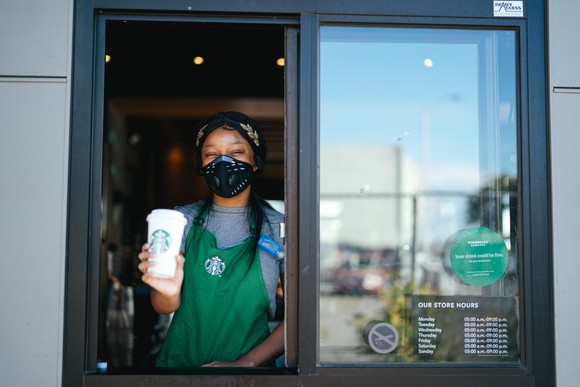 A Starbucks employee at a drive thru handing out a drink. 