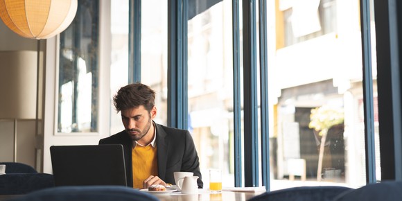Man works on laptop while sitting at cafe table.