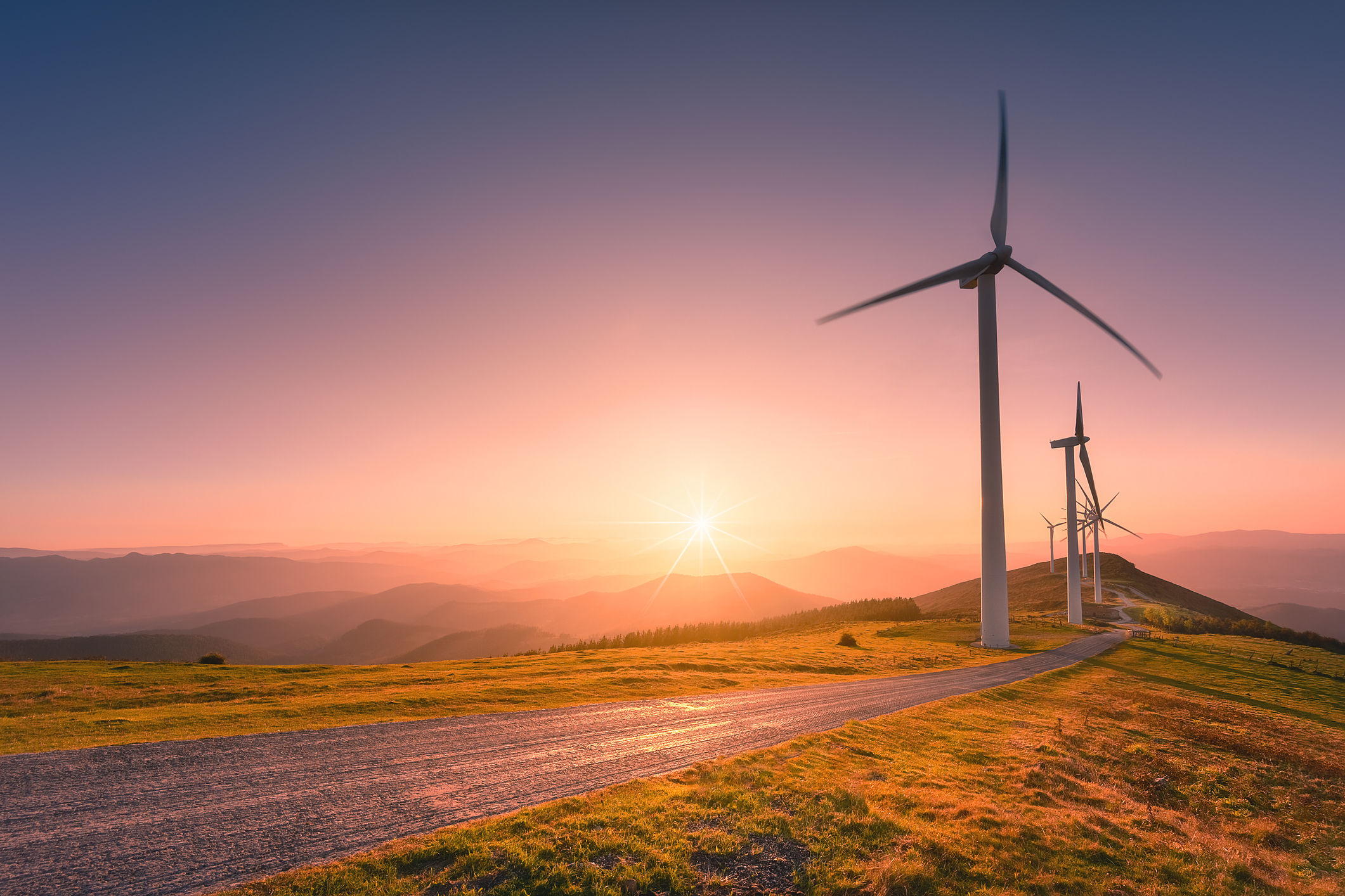 Wind turbines along a road with the sun setting in the background.