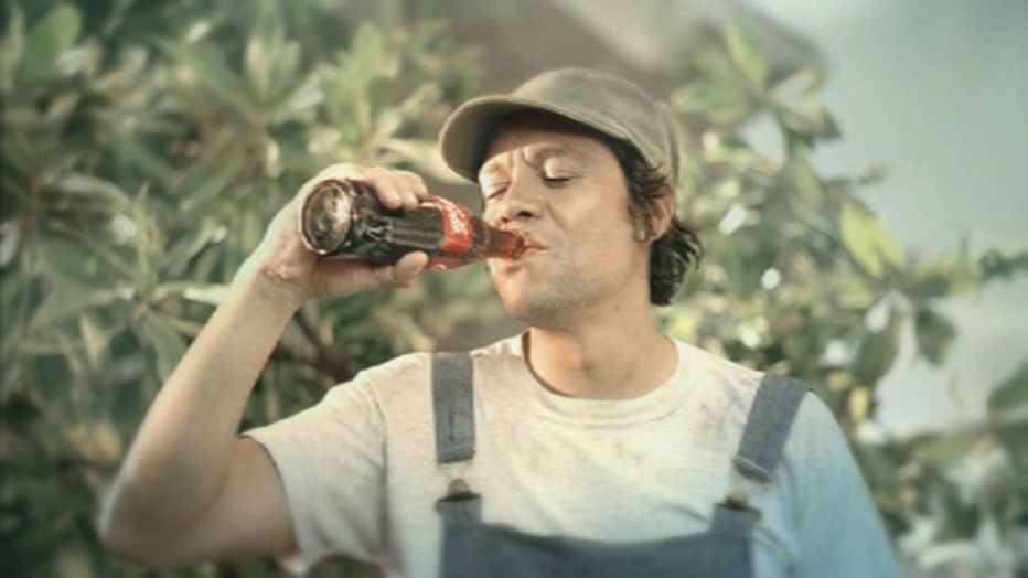 A man wearing overalls drinking from a Coca-Cola bottle.