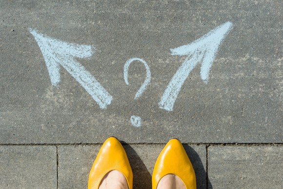 Woman's standing on sidewalk, choosing between two chalk arrows pointing in opposite directions. 