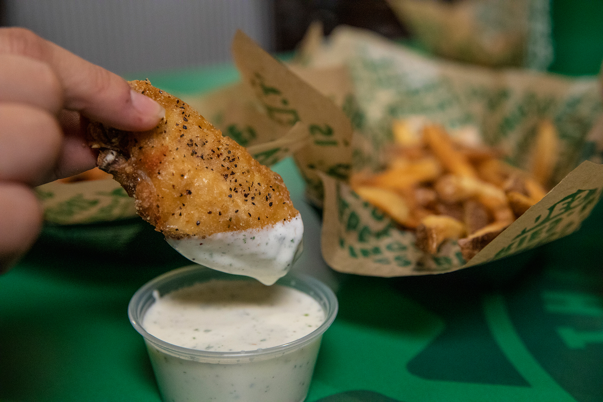 A person dips a chicken wing into ranch dressing.