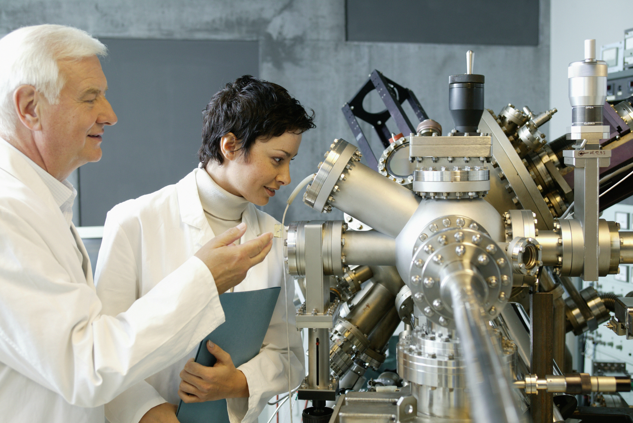 Two people observe manufacturing equipment.