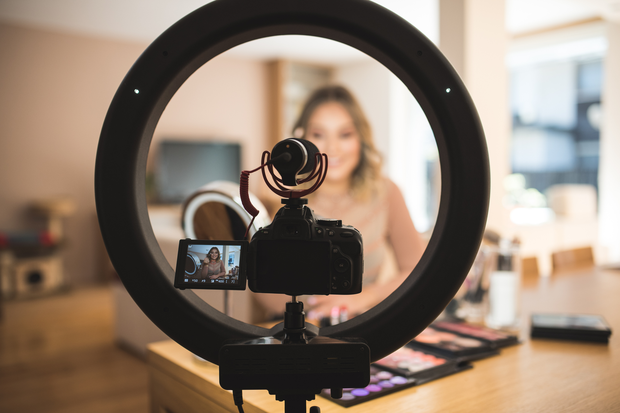 An internet personality speaks into a small camera in front of a ring light,.