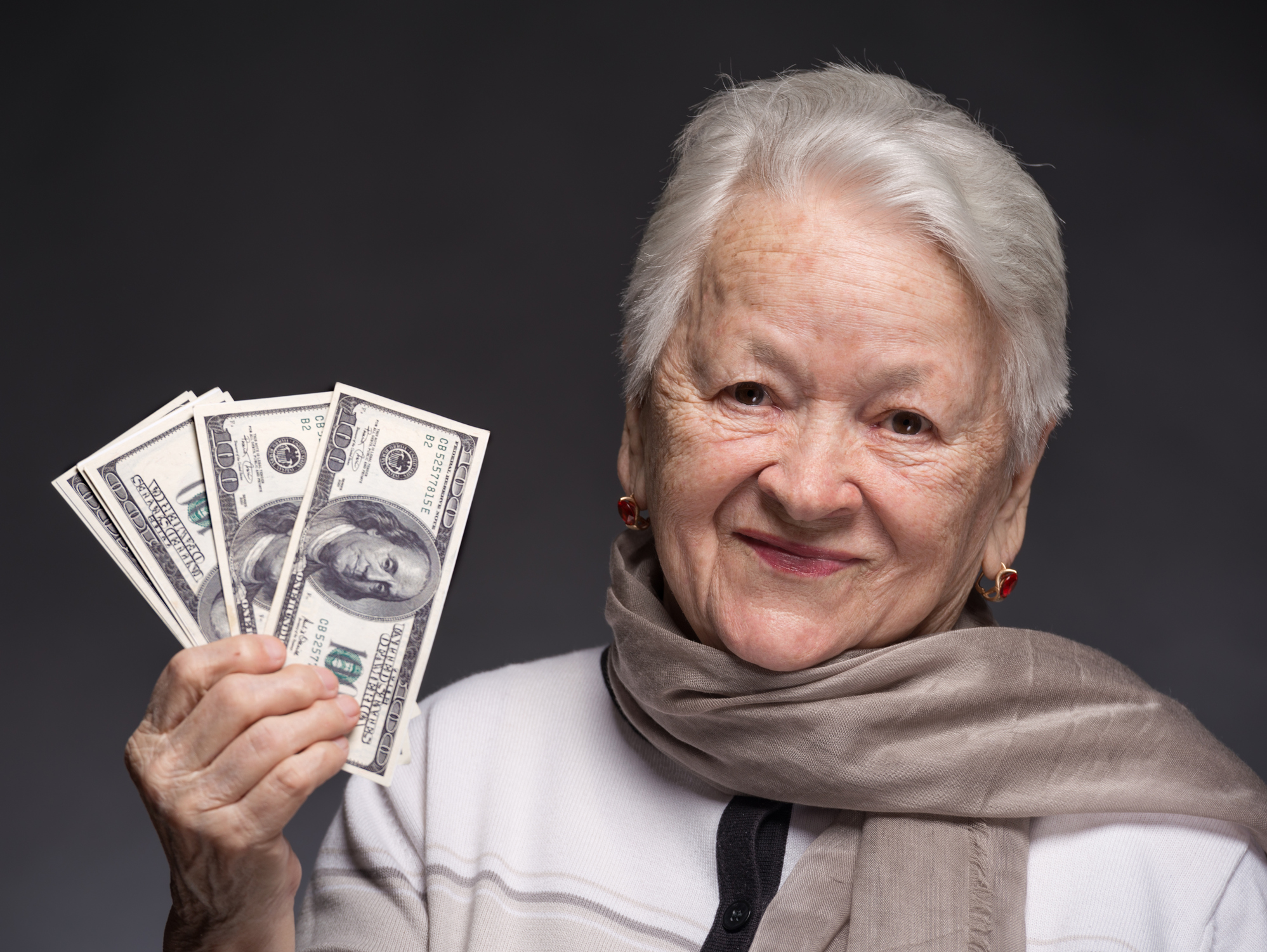 A stylish older woman is holding some cash and smiling.