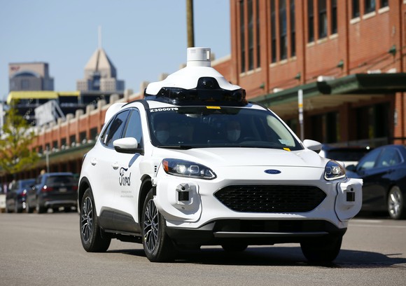 A white Ford Escape Hybrid with visible self-driving sensors, including a lidar unit on its roof.