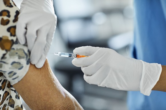 Gloved hands deliver a shot to a patient's arm.