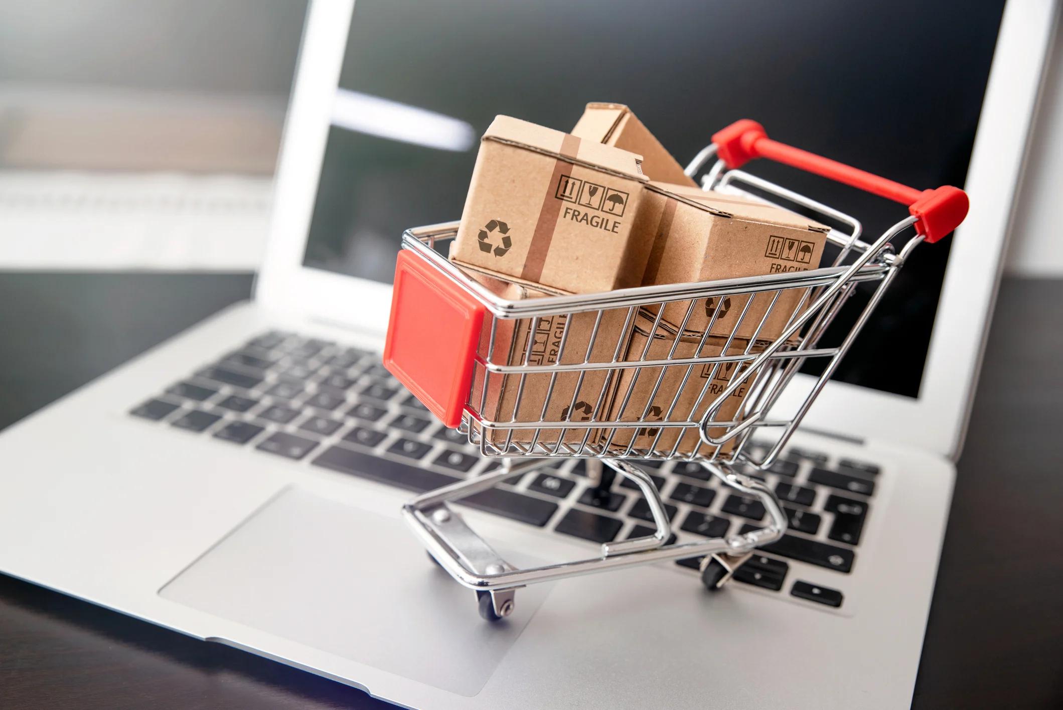 Miniature shopping cart full of boxes on top of a laptop keyboard