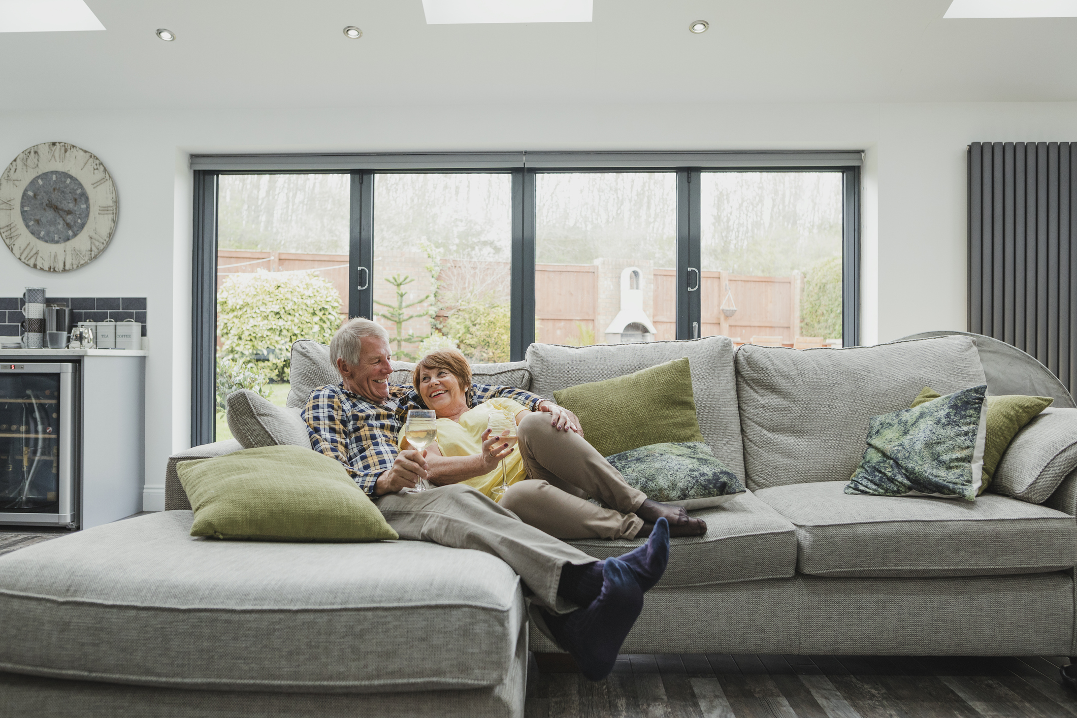 An older man and woman lounging on a couch, holding wine glasses.