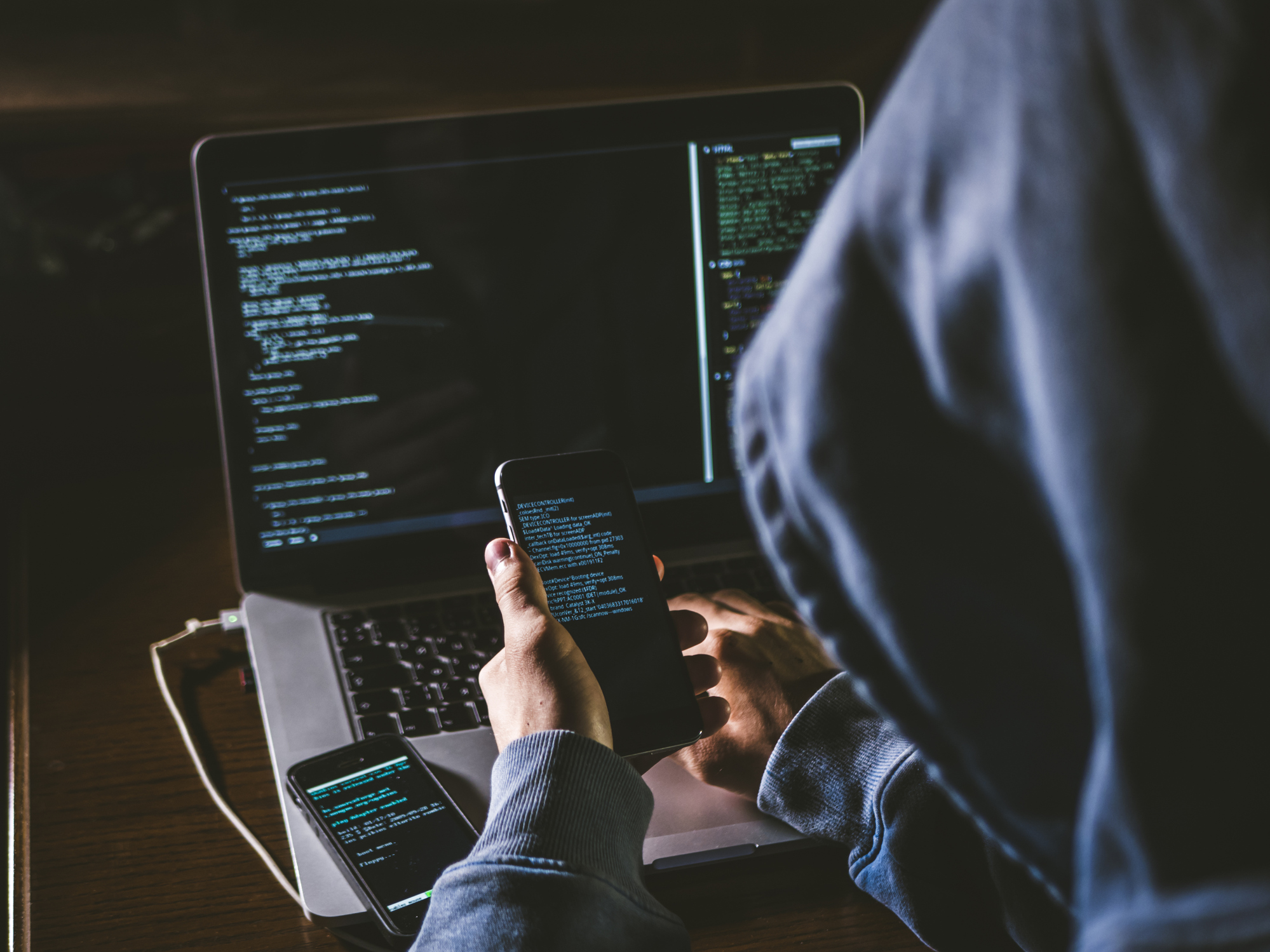 A hooded hacker using phones and a PC.