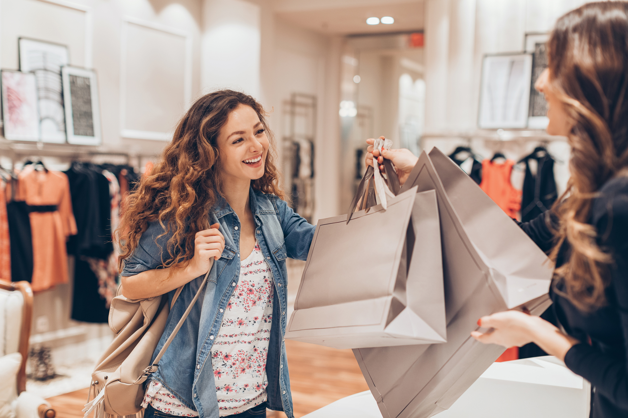 A female clerk handing two shopping bags to a female customer in a department store