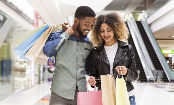 Two people with shopping bags standing in a mall.