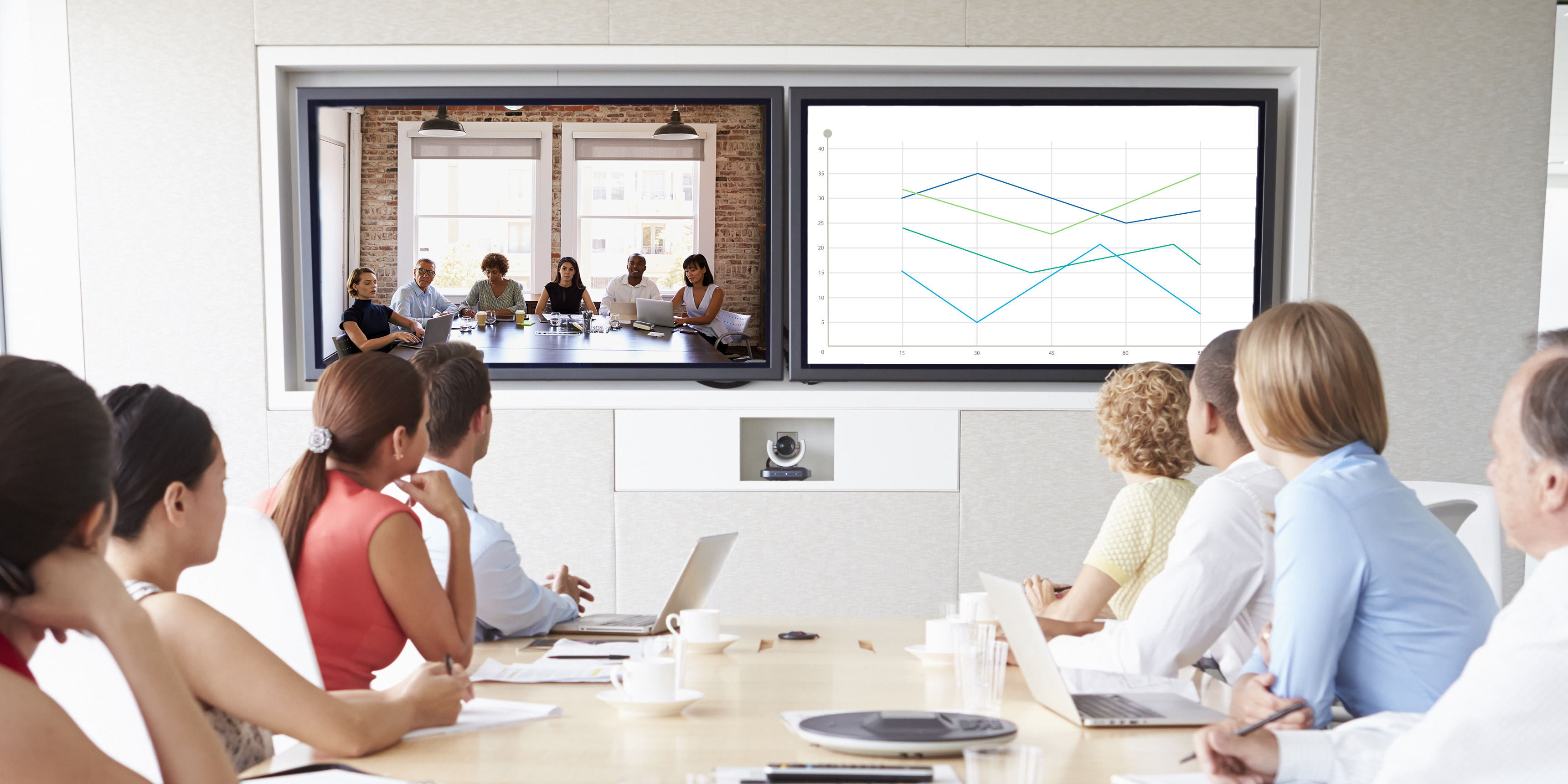 Businesspeople gathered around conference table, interacting with remote group on Zoom