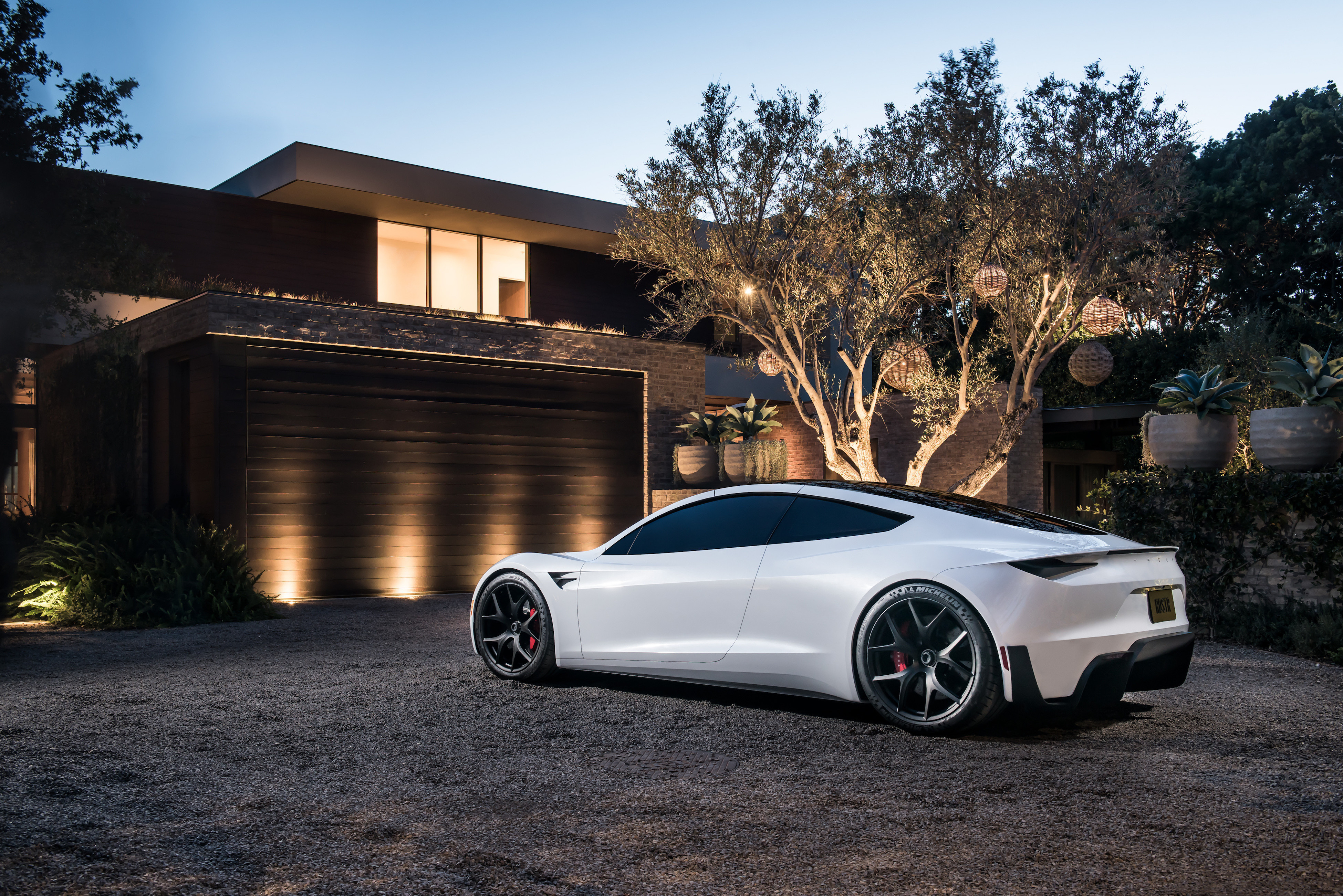 White Tesla Roadster parked outside a house at twilight.
