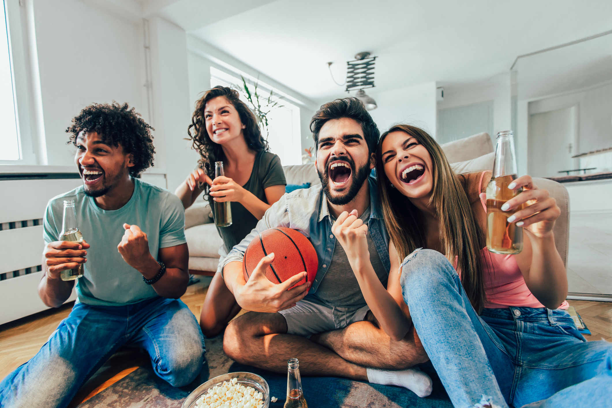 A group of friends drinking beer cheering in a home. One of them is holding a basketball.