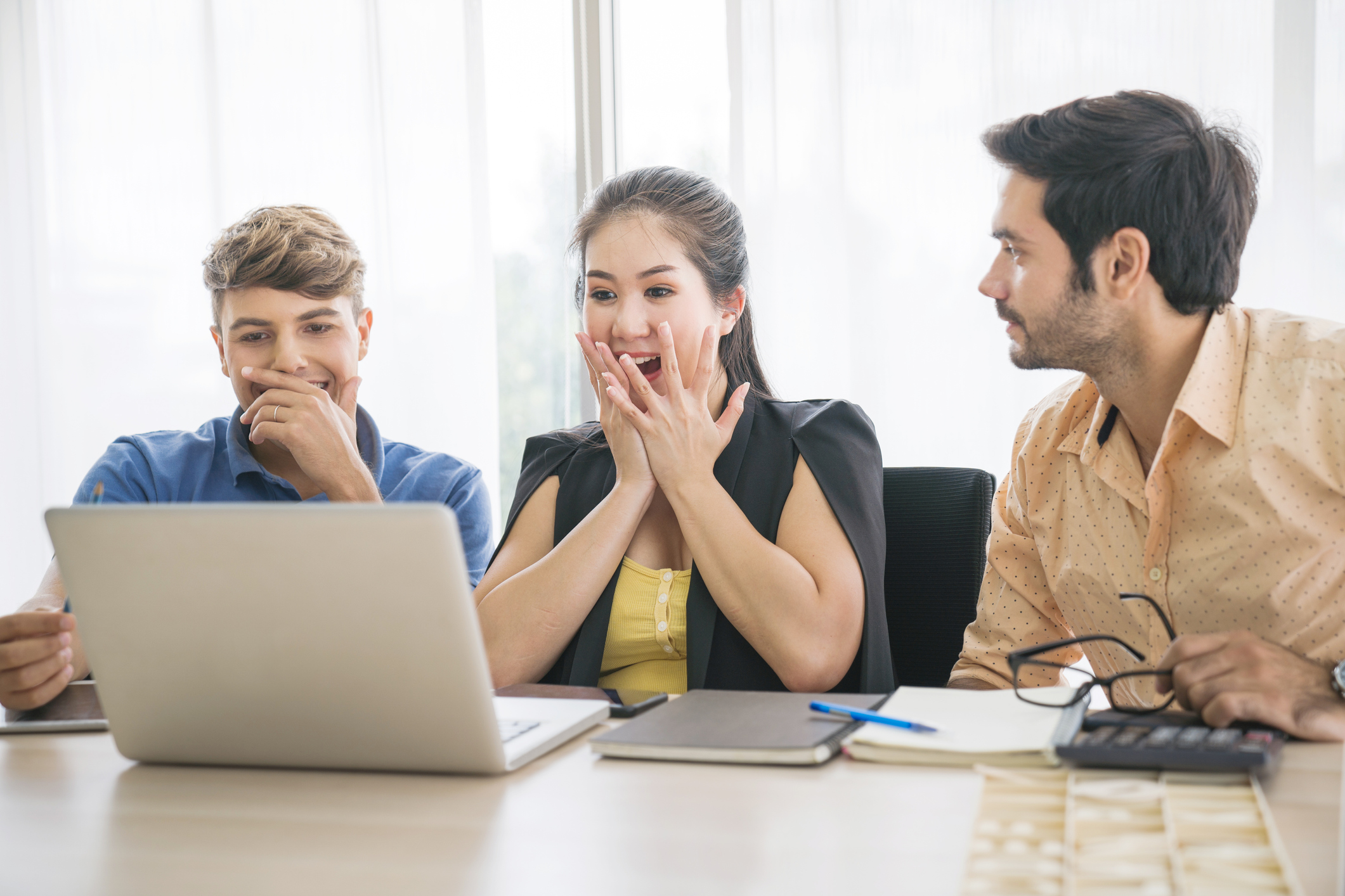 Three young workers excitedly look at a laptop screen in conference room.