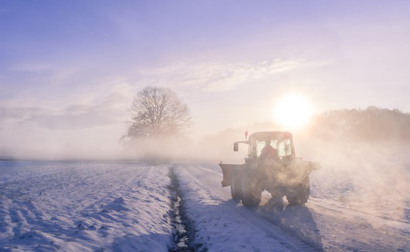 A tractor plows a snowy field around sunrise.