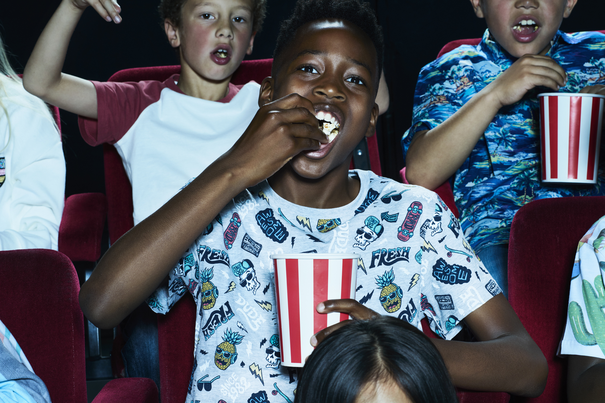 Kids watching a movie in a theater and eating popcorn.