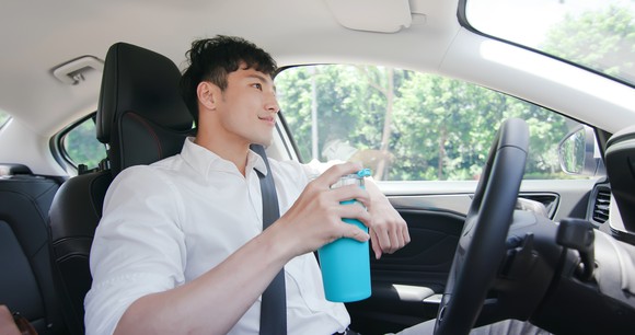 Relaxed person with a mug in their right hand rides in an autonomous self-driving car on road.