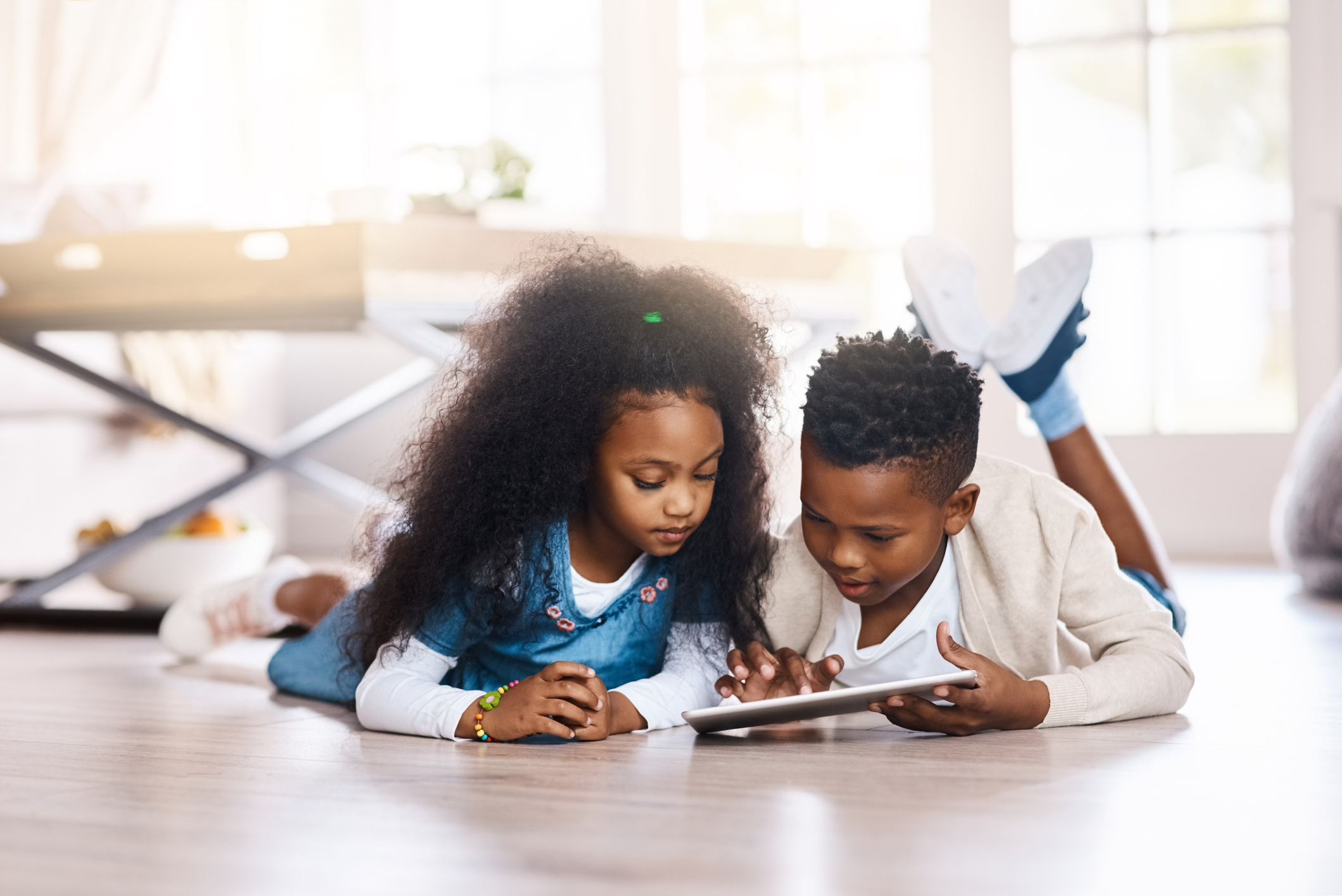 Two kids laying on the floor playing on a tablet.