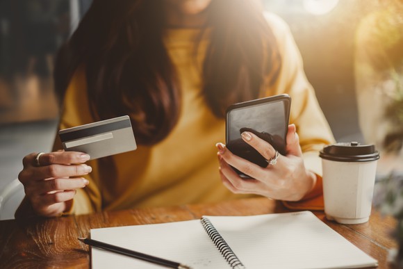 A woman holds a smartphone in one hand and her credit card in the other.