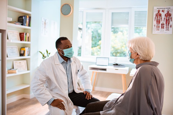 Patient, wearing a mask, conferring with a doctor, similarly masked.