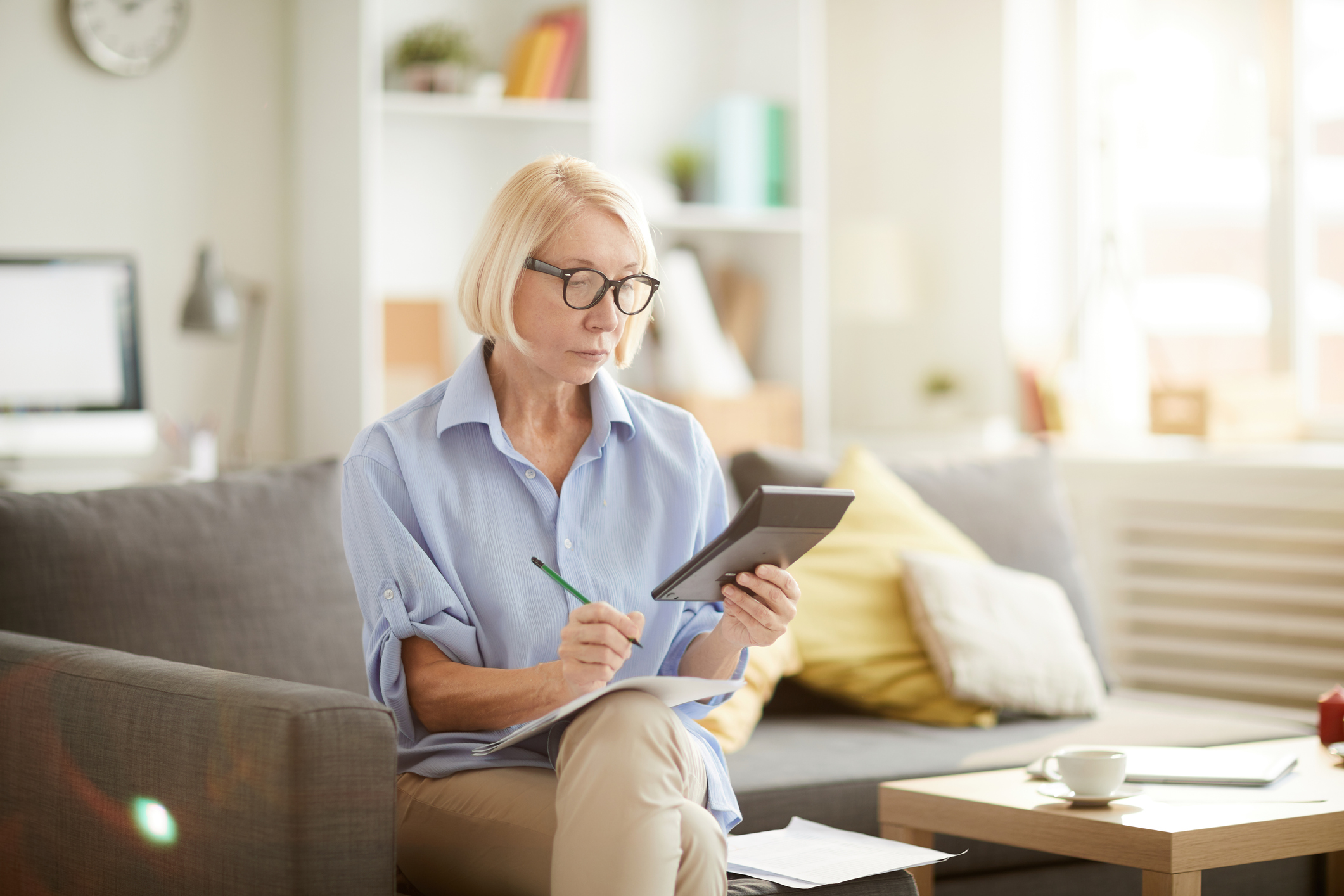 Older person sitting on a couch looking at a calculator