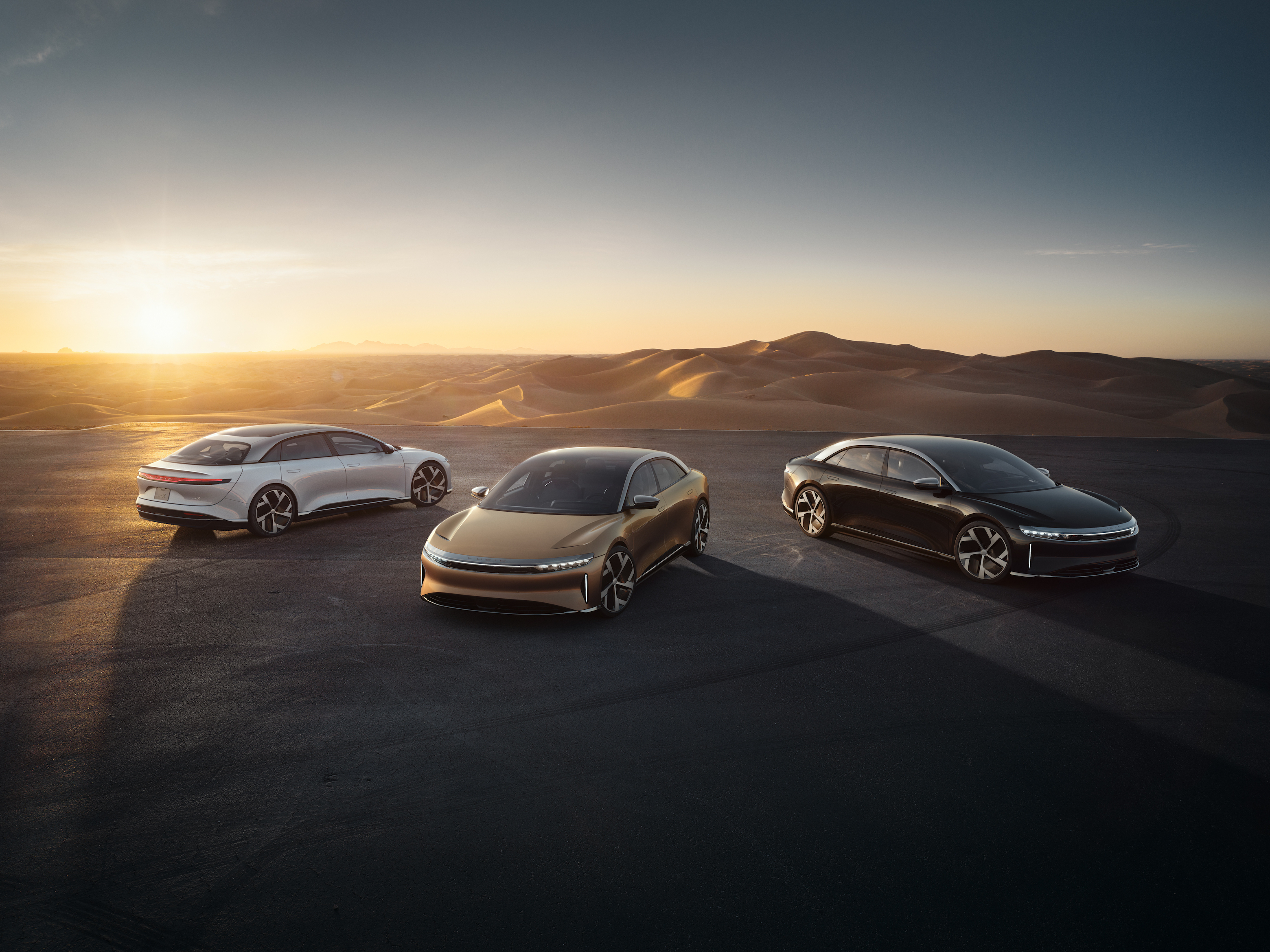 Various trims of the Lucid Air luxury sedan in the desert at sunrise.
