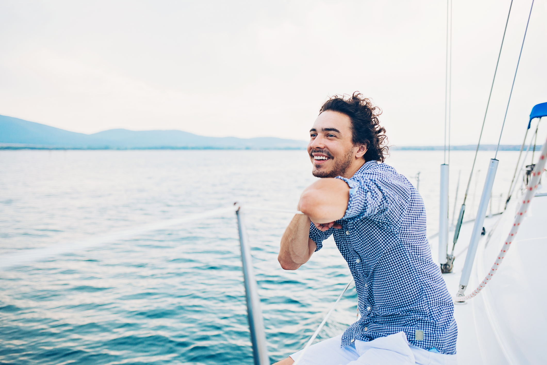 A happy smiling person sailing on beautiful blue waters against backdrop of mountains.