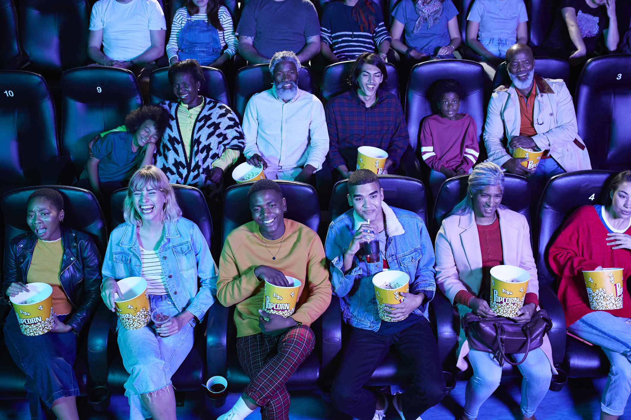 Several happy people watching a movie and eating popcorn in a theater.