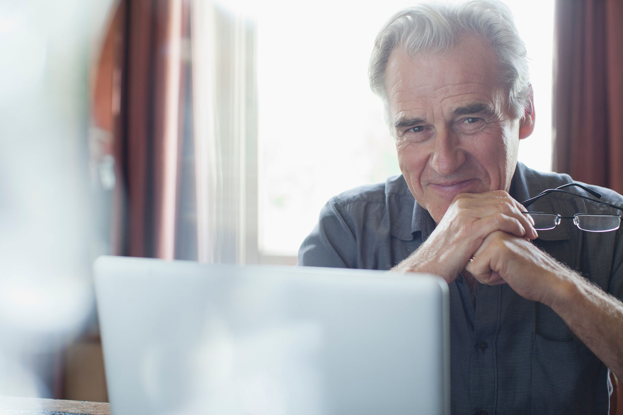 A senior man smiling as he uses a laptop computer.