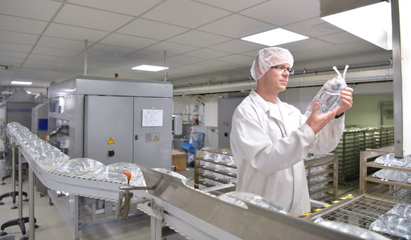 Technician studying sterile vaccine bag on assembly line.