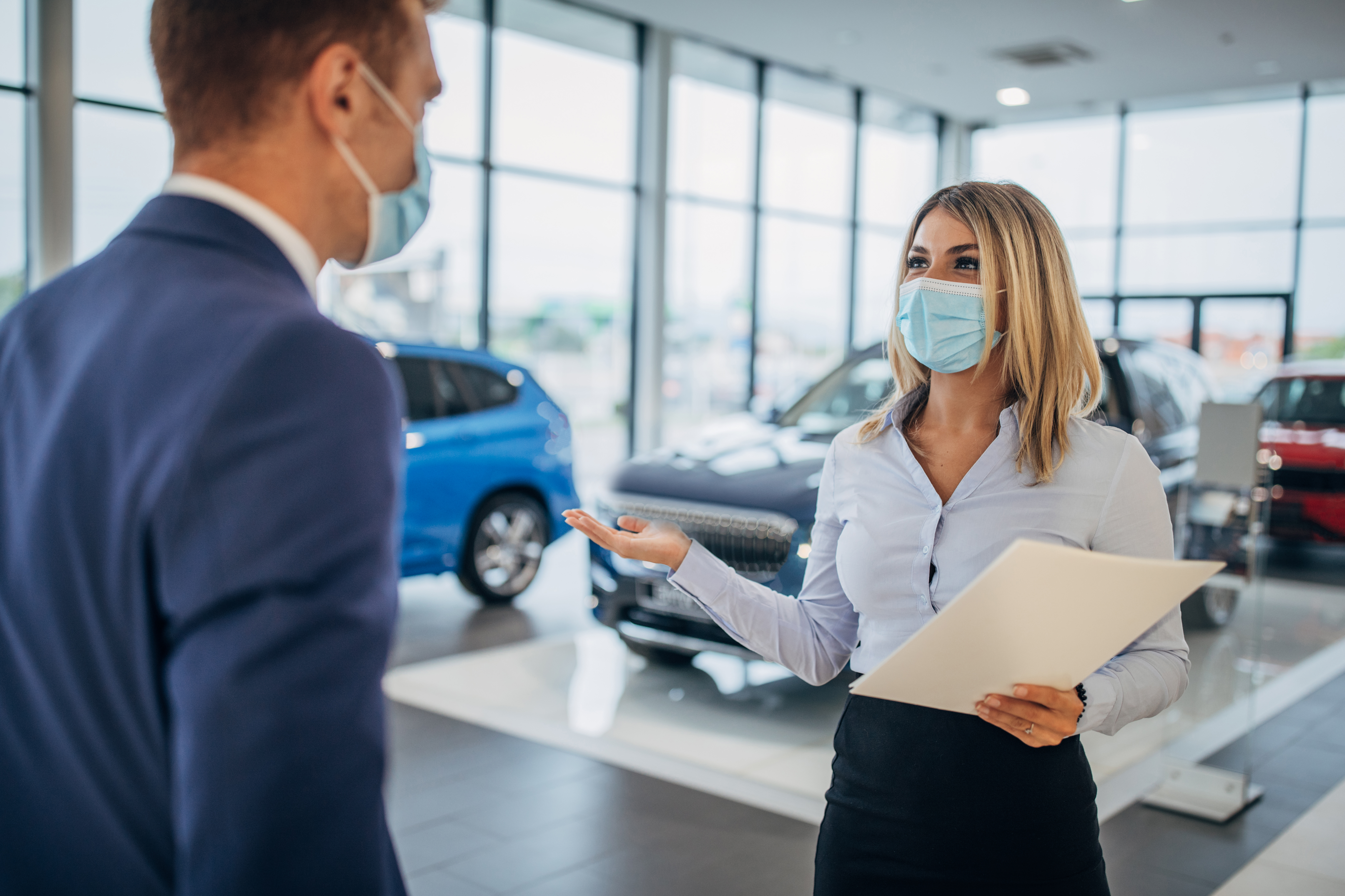 A masked car salesperson discussing a car with a masked customer.