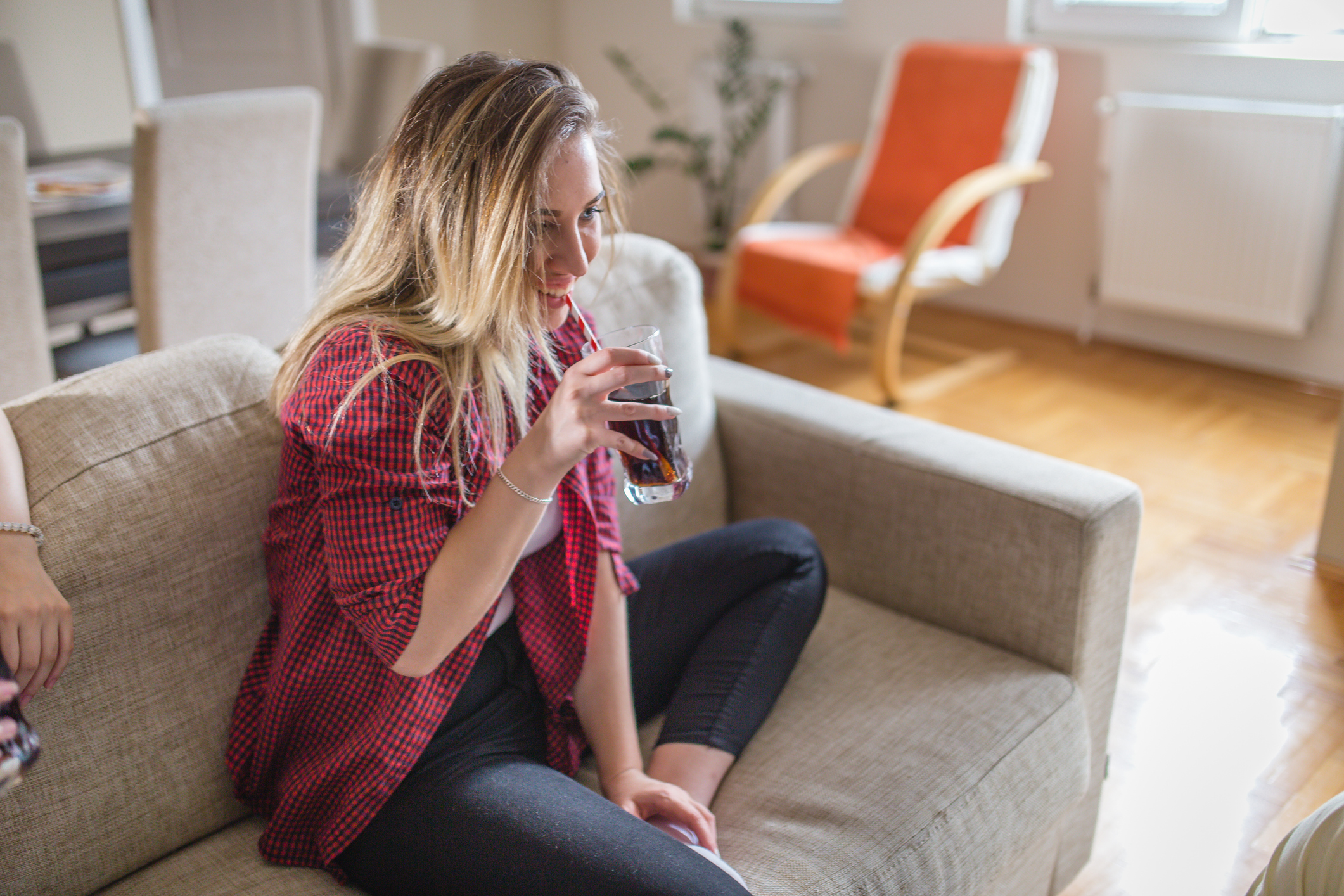 A woman sitting on a couch and drinking a glass of cola.