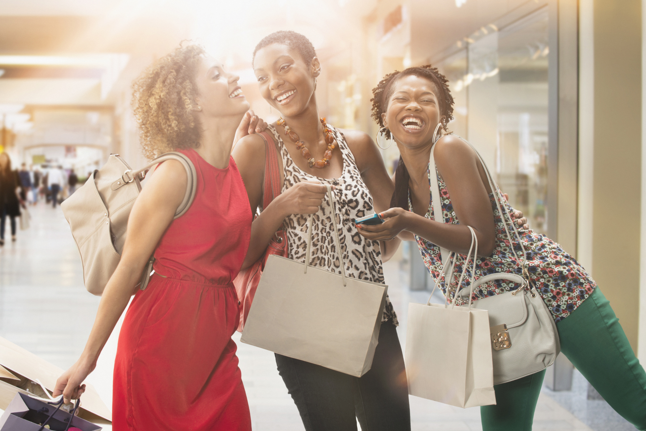 Three women at a shopping center holding shopping bags and smiling.