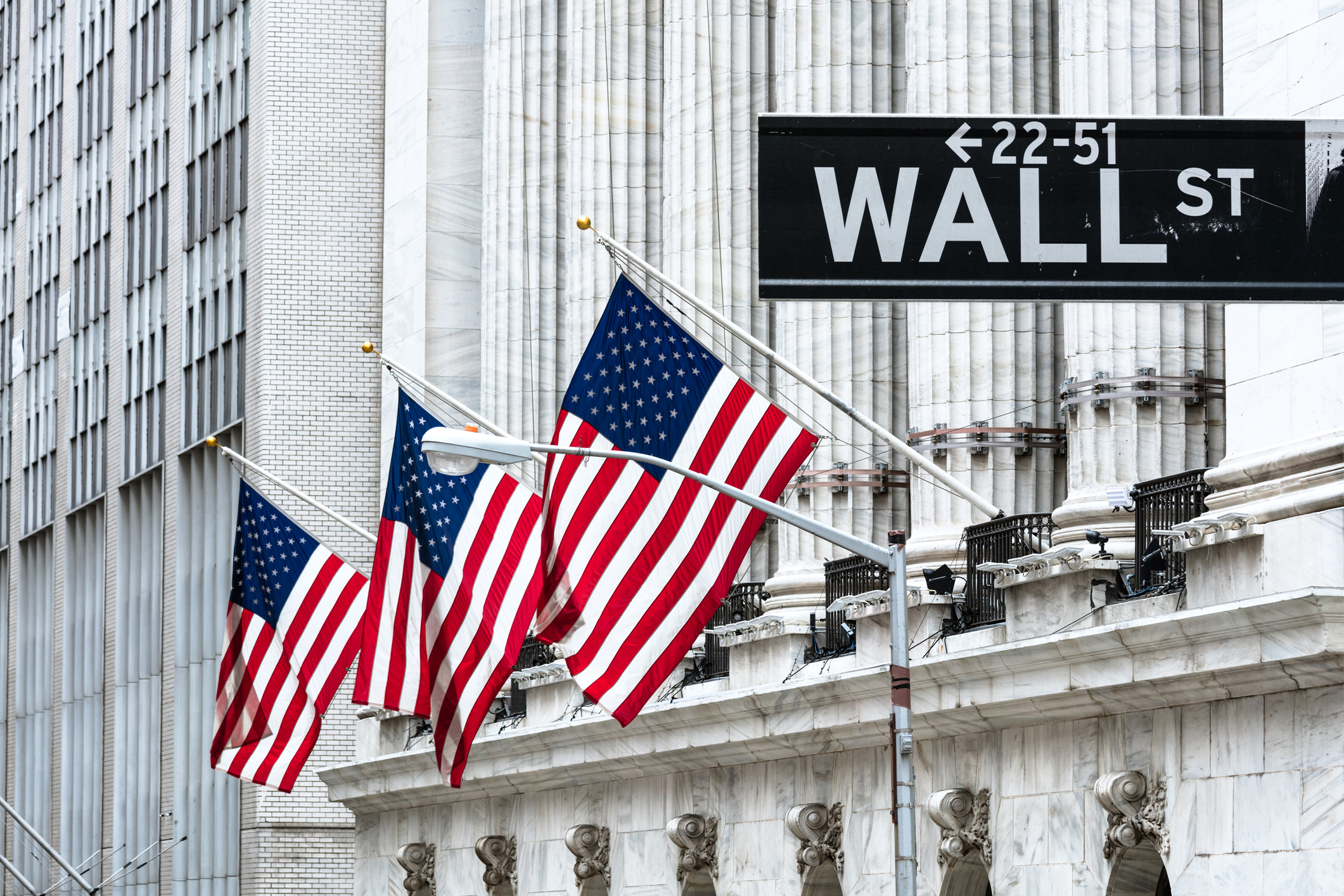American flags outside NYSE with Wall Street sign.