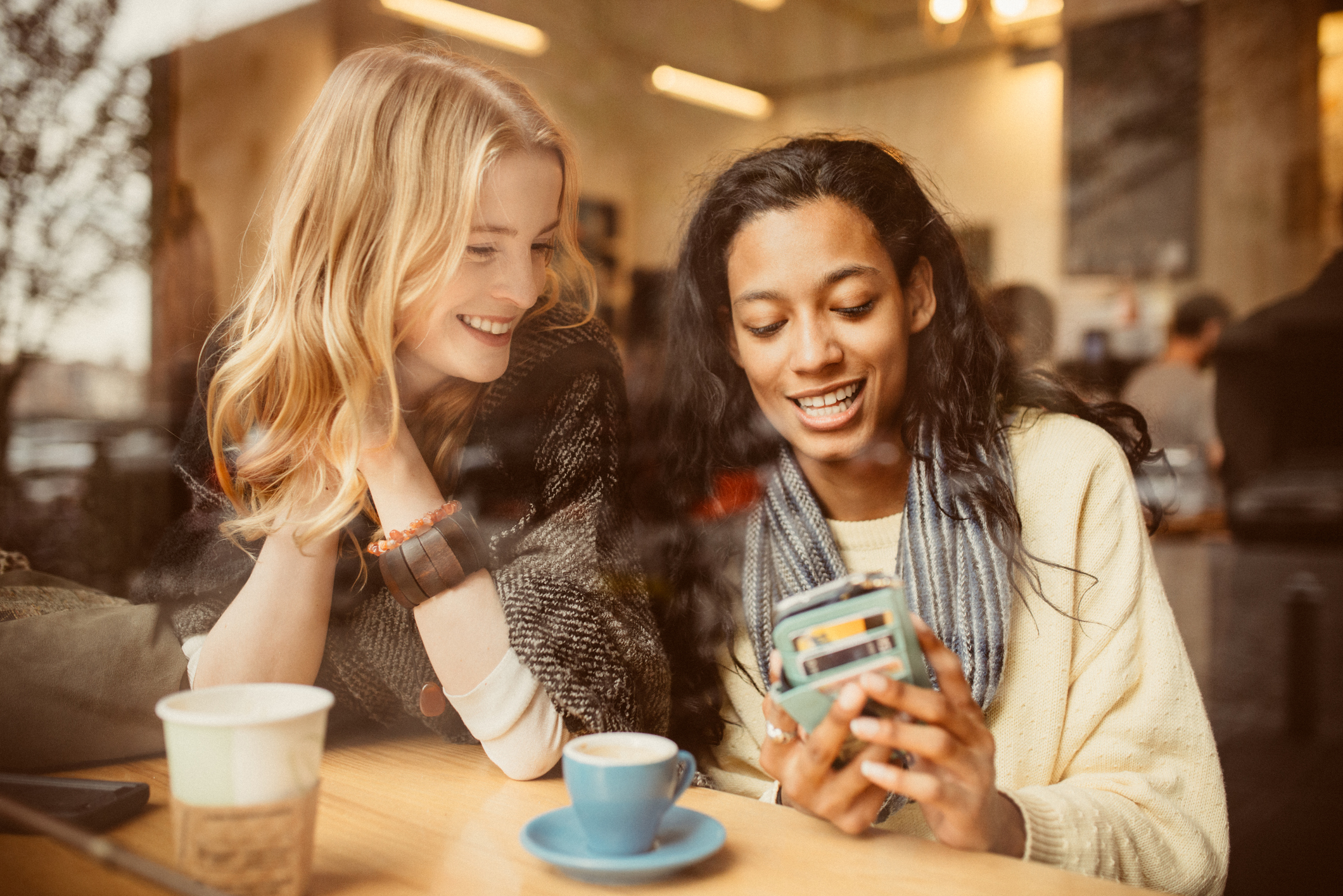 Two people at a table with coffee cups looking at a mobile phone.
