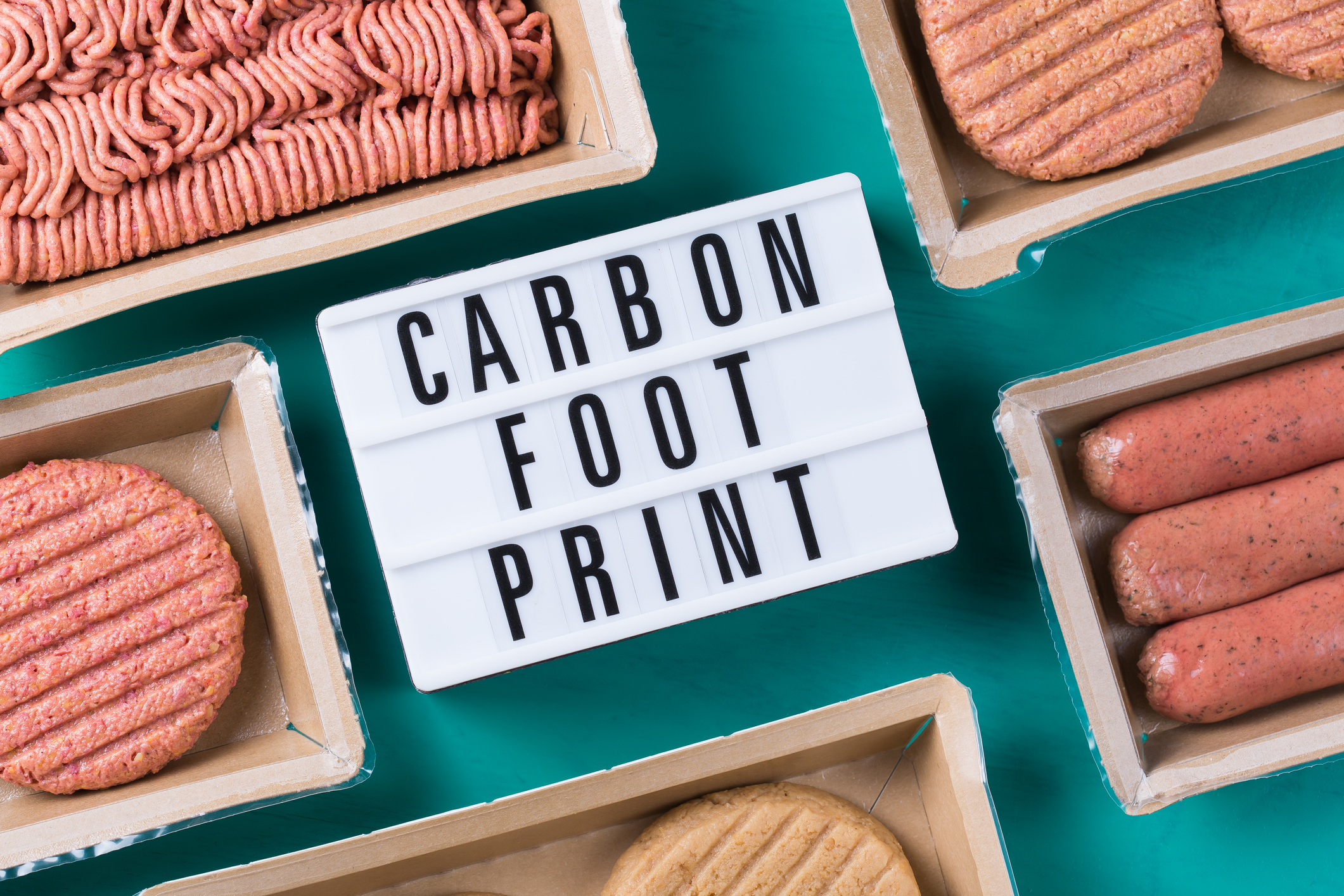 Various items of plant-based meat on a teal tabletop, surrounding a sign reading "Carbon Footprint."