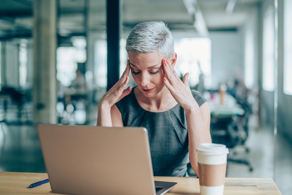 An investor rubs her temples as she looks at her computer in an office setting. 