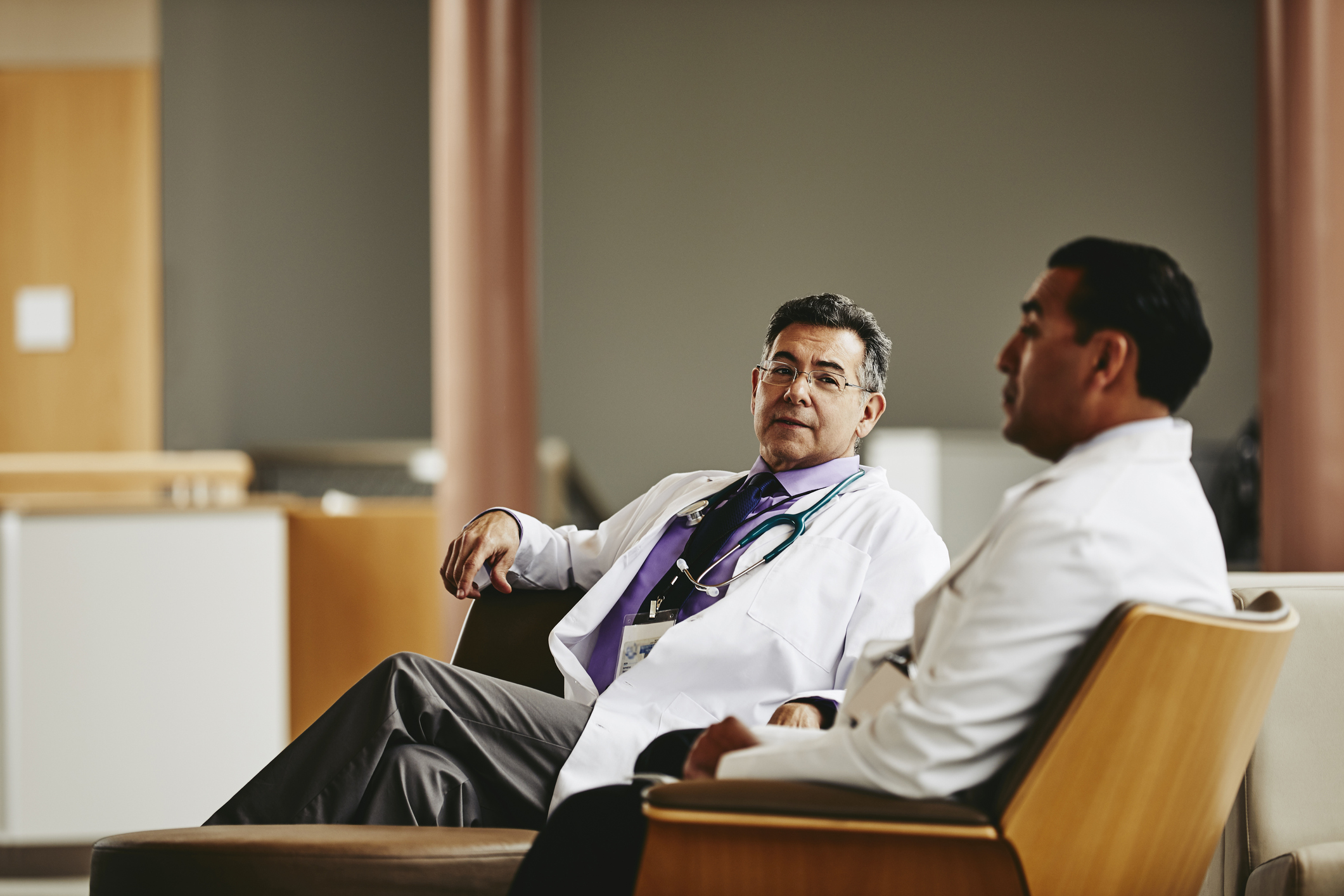 Two doctors chat while sitting in a hospital waiting room.