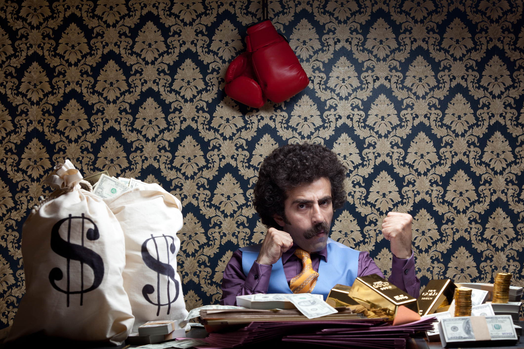 Person making fists in office with boxing gloves over their head and money bags on their desk.