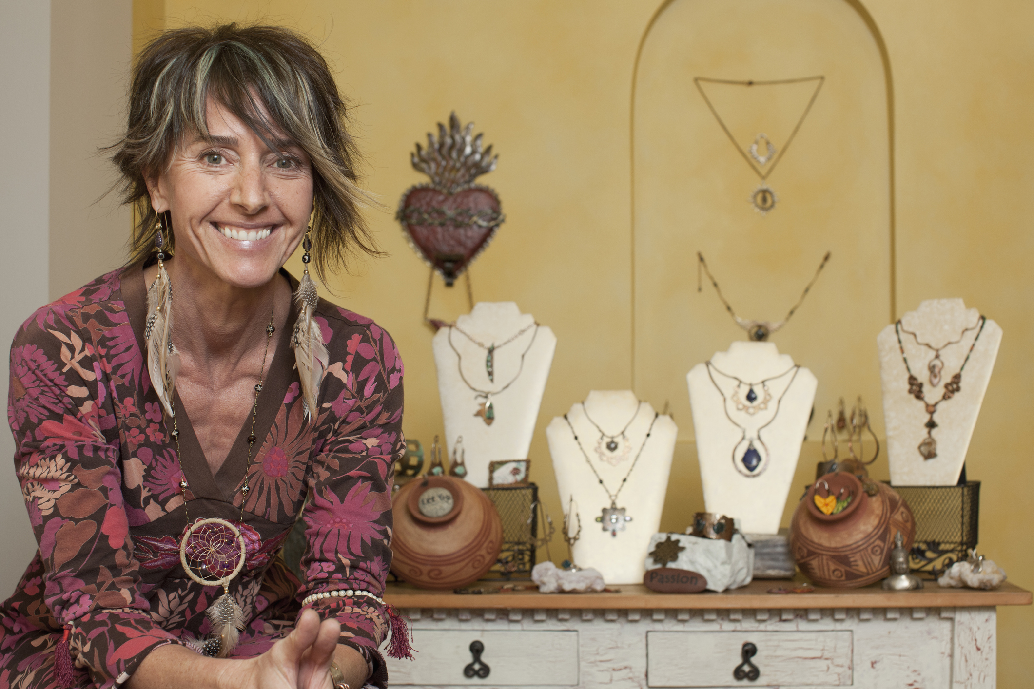 A middle aged woman smiles outside her jewelry display booth.
