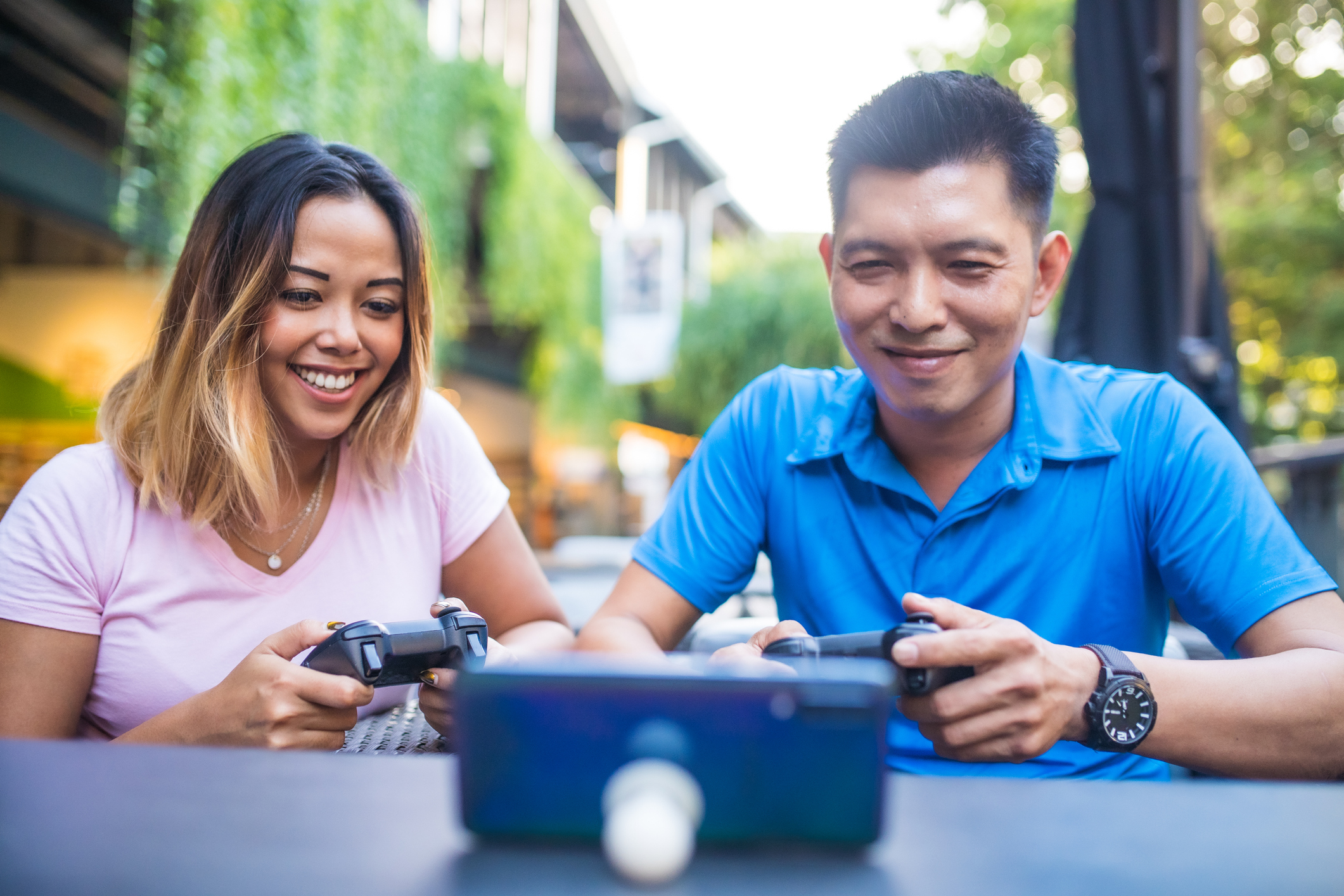 Two people play a mobile game using controllers, with the mobile phone propped up on a table.