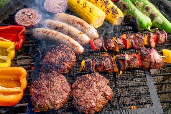 A charcoal grill cooking a colorful selection of meat and vegetables.